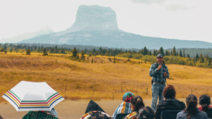 Lauren Monroe Jr speaking during the Wayfinders Circle Gathering on Blackfeet Territory Montana with Chief Mountain in the background